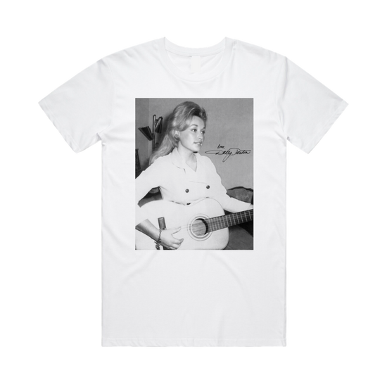 Official Dolly Parton Merchandise. 100% white premium cotton t-shirt with a black and white photo of young Dolly Parton in a white button blazer playing an acoustic guitar.